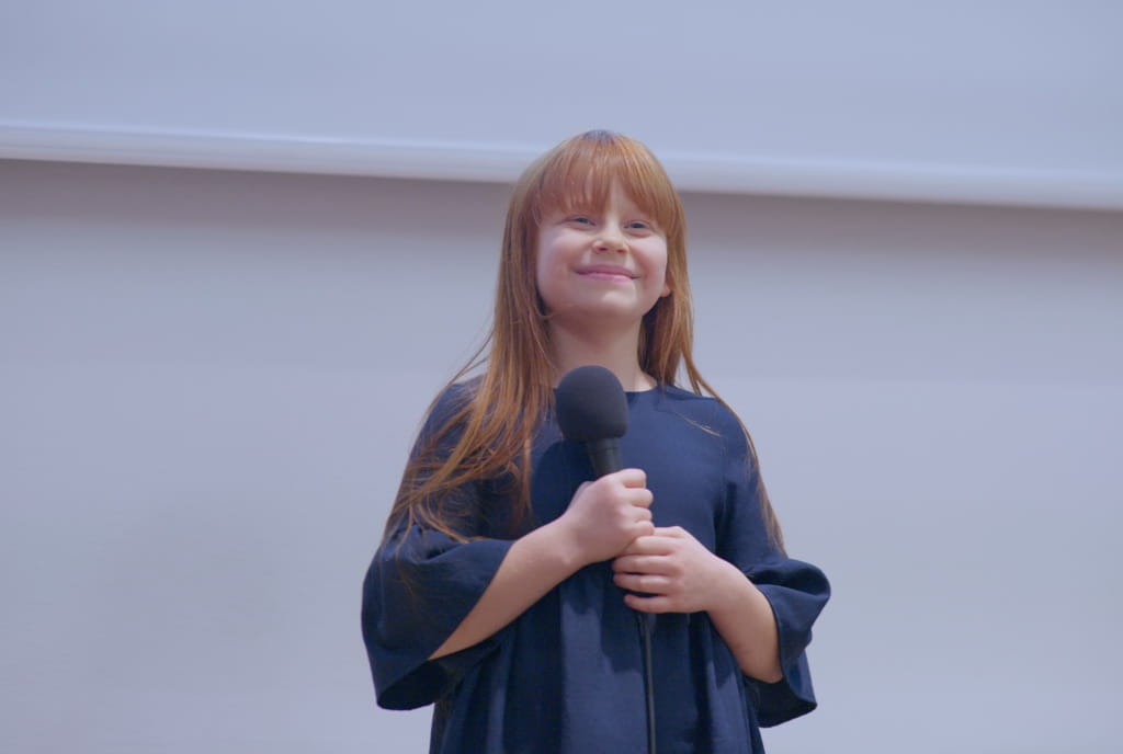 Uśmiechnięta dziewczynka w wieku około 10 lat trzymająca mikrofon 