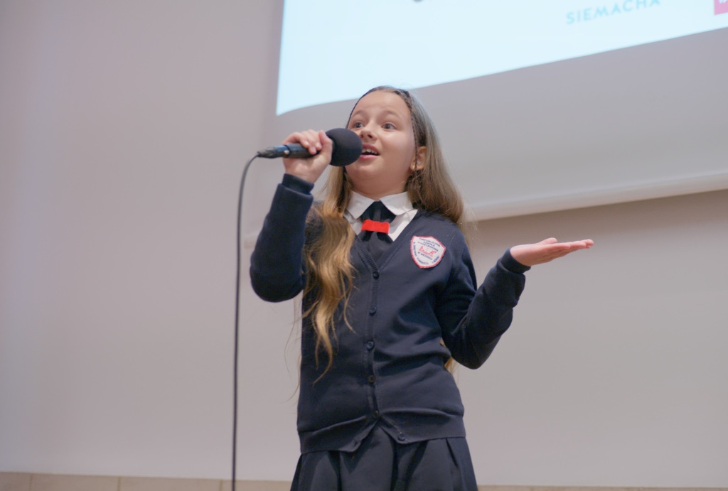 Dziewczynka w wieku około 10 lat, śpiewająca do mikrofonu na białym tle 