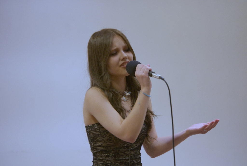 Dziewczynka w wieku około 14 lat, śpiewająca do mikrofonu na białym tle 