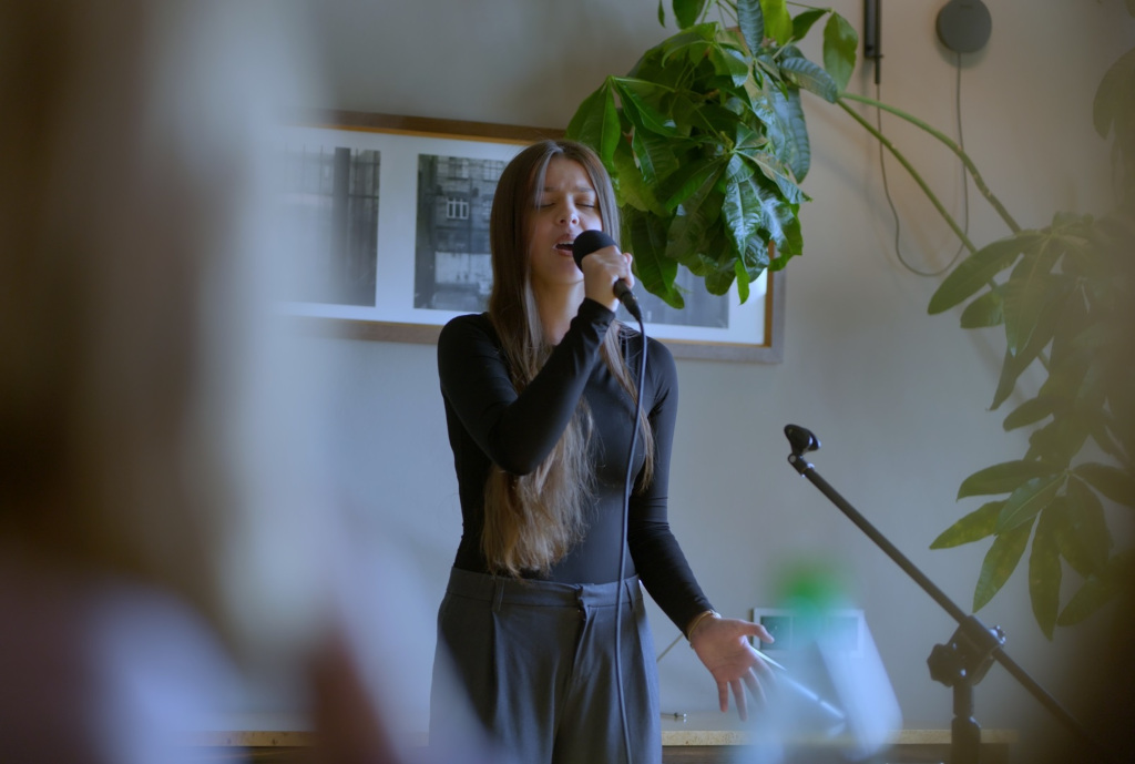 Dziewczynka w wieku około 11 lat śpiewająca do mikrofonu na tle rośliny i obrazu