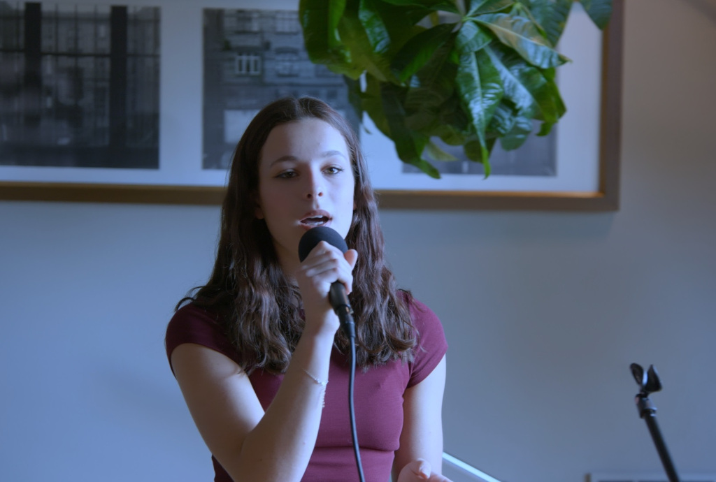 Dziewczynka w wieku około 13 lat śpiewająca do mikrofonu na tle ram ze zdjęciem