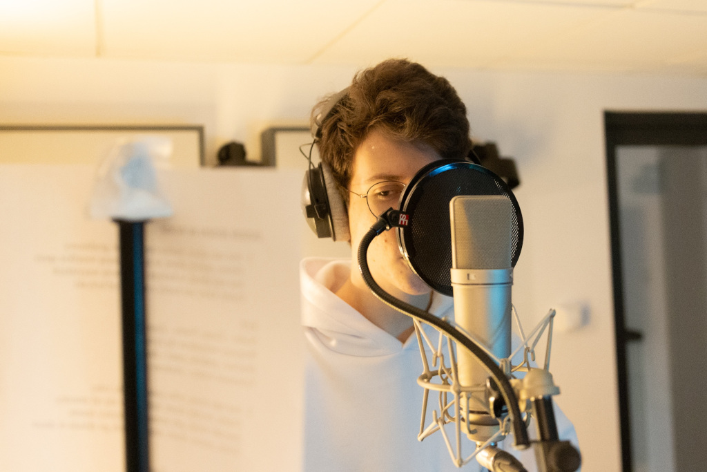 Studio nagraniowe, chłopiec przed mikrofonem patrzący na tekst piosenki 