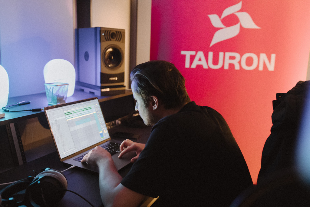 Studio nagraniowe, producent muzyczny przed laptopem, za nim banner TAURON