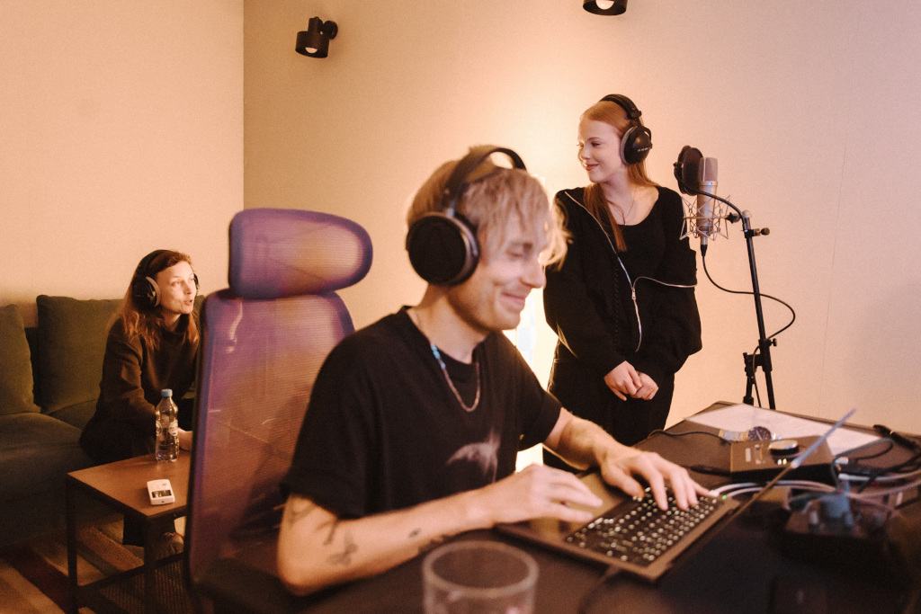 Studio nagraniowe, producent muzyczny przed laptopem, za nim dziewczynka przed mikrofonem 