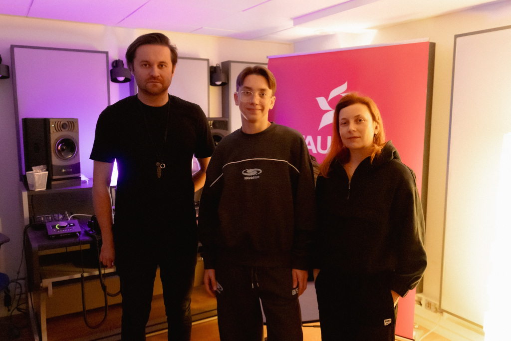 Studio nagraniowe, producent muzyczny przed laptopem, za nim chłopiec i banner TAURON 