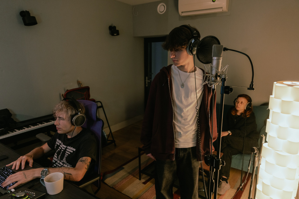 Studio nagraniowe, na pierwszym planie chłopiec przed mikrofonem, obok niego siedzi producent muzyczny 