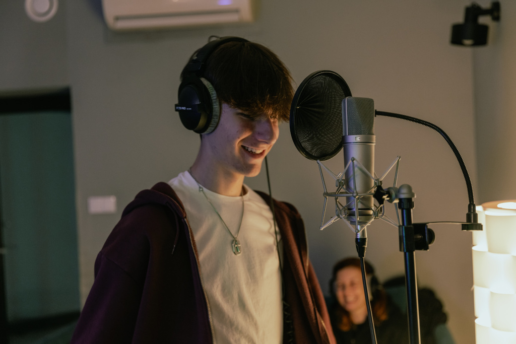 Studio nagraniowe, na pierwszym planie uśmiechnięty chłopiec przed mikrofonem