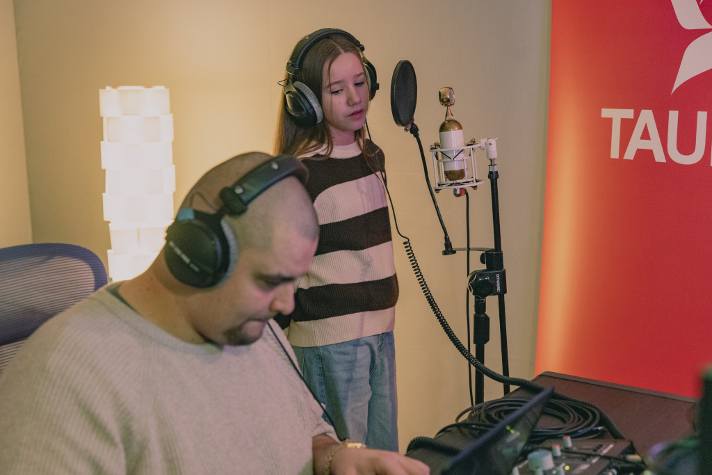 – Studio nagraniowe, na pierwszym planie producent muzyczny, za nim dziewczynka przed mikrofonem